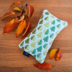 A small cedar pouch sitting on a wooden tabletop with fir tree handwoven design.  Around the pouch are some autumnal leaves.